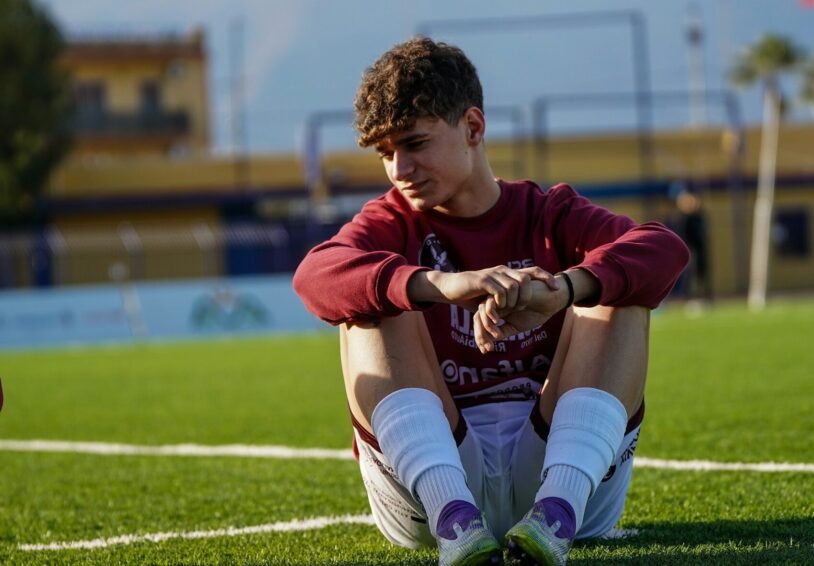 Jongen met voetbalkleding zit verdrietig op het gras