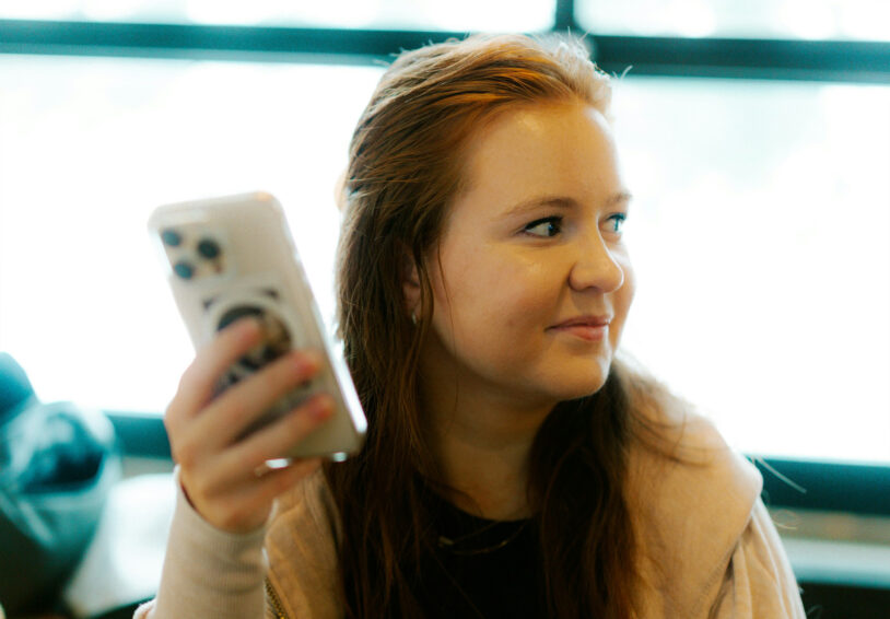 Tienermeisje met telefoon in haar hand die verlegen opzij kijkt