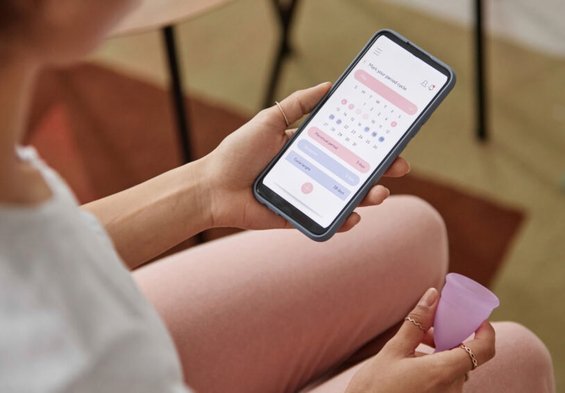 Foto bij onderzoek over cyclus app als anticonceptie met vrouw met telefoon en menstruatiecup in haar hand